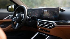 Interior view of a modern BMW car showcasing the steering wheel and wide dashboard display with digital driving information and a rear-view camera feed.