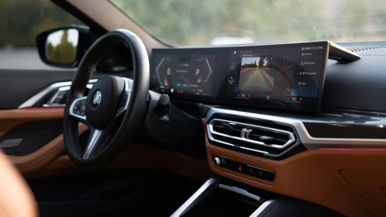 Interior view of a modern BMW car showcasing the steering wheel and wide dashboard display with digital driving information and a rear-view camera feed.