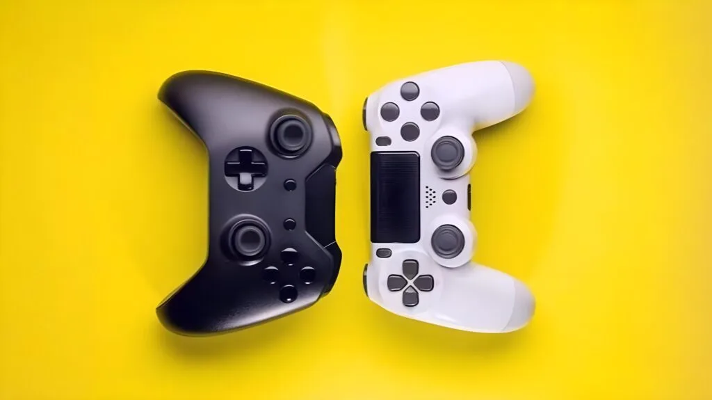 Black Xbox controller and white PlayStation controller placed side by side on a bright yellow background, highlighting modern gaming hardware.
