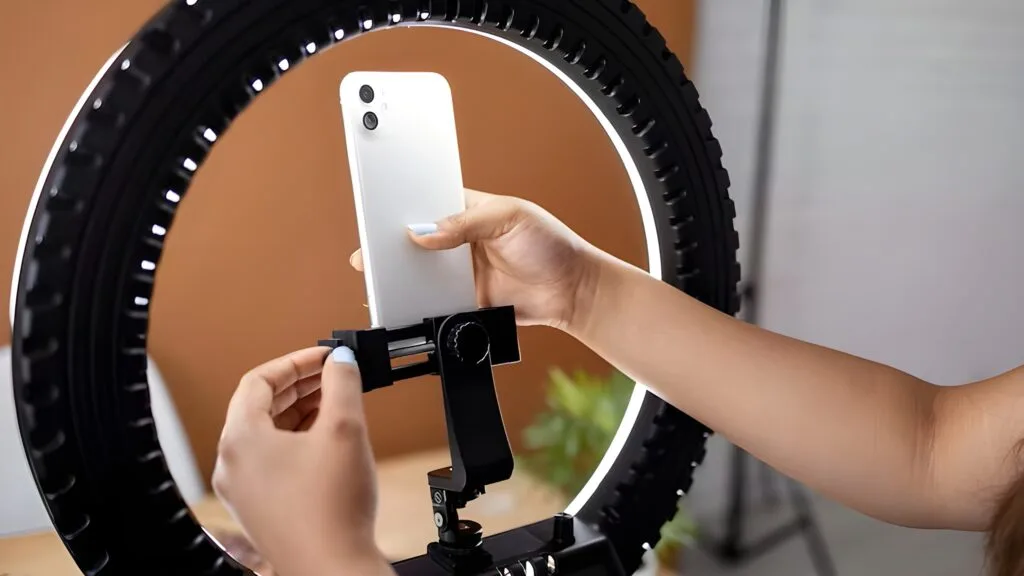 Beginner vlogger recording a makeup tutorial using a smartphone on a tripod with basic lighting and makeup products on the desk.